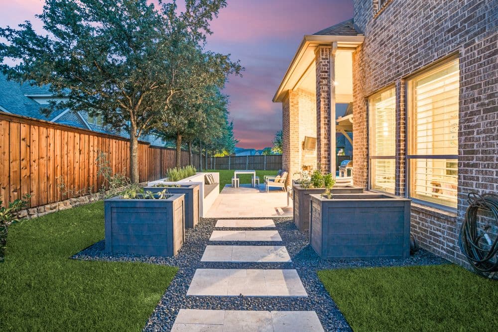 Modern backyard patio with stone walkway, planters, and lush green grass at sunset.