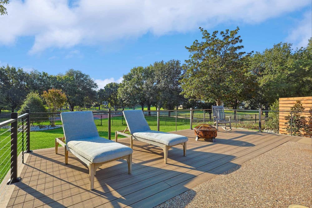 Outdoor patio with two lounge chairs, green lawn, and blue sky in a serene setting.