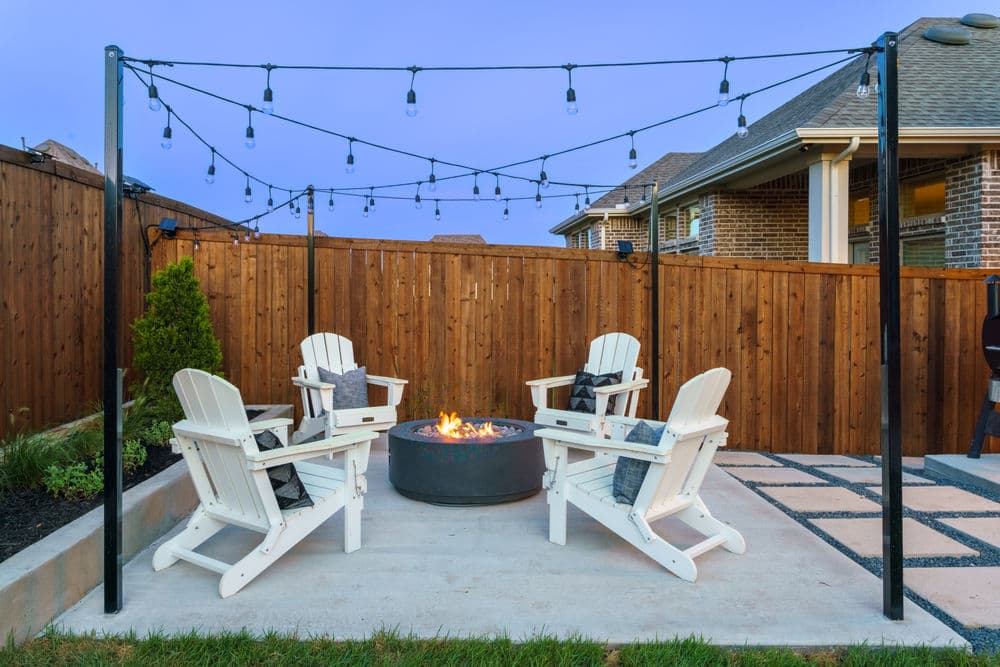 Cozy outdoor fire pit area with white chairs and string lights in a private backyard.
